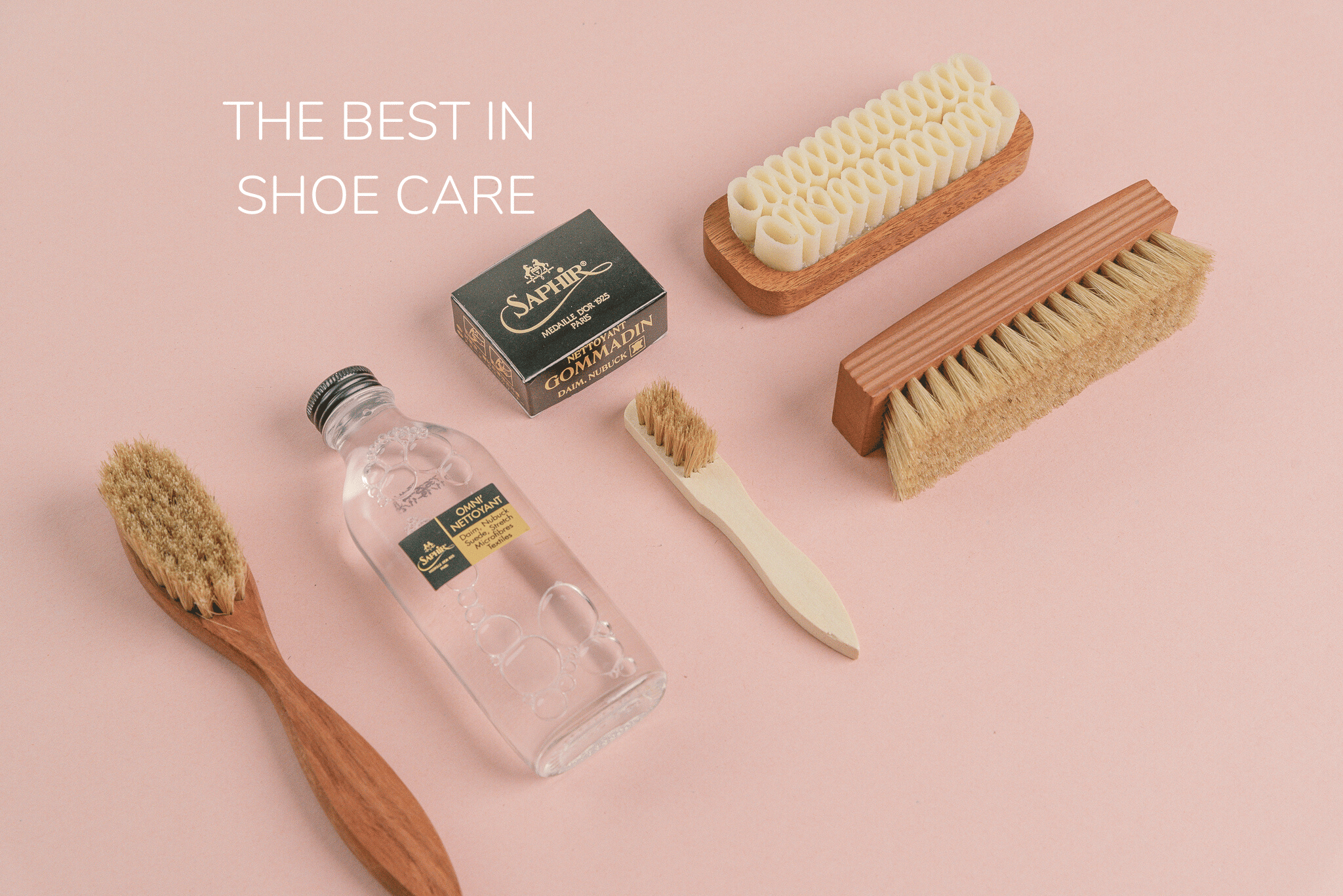Aerial shot of Saphir Medaille d'or horse hair spatula brush, Saphir Medaille d'or Omni Nettoyant suede shampoo, Saphir Medaille d'or Crepe suede brush, Saphir Medaille d'or Gommadin suede eraser brick, Saphir Medaille d'or Horse hair polishing and shining brush on pink background 